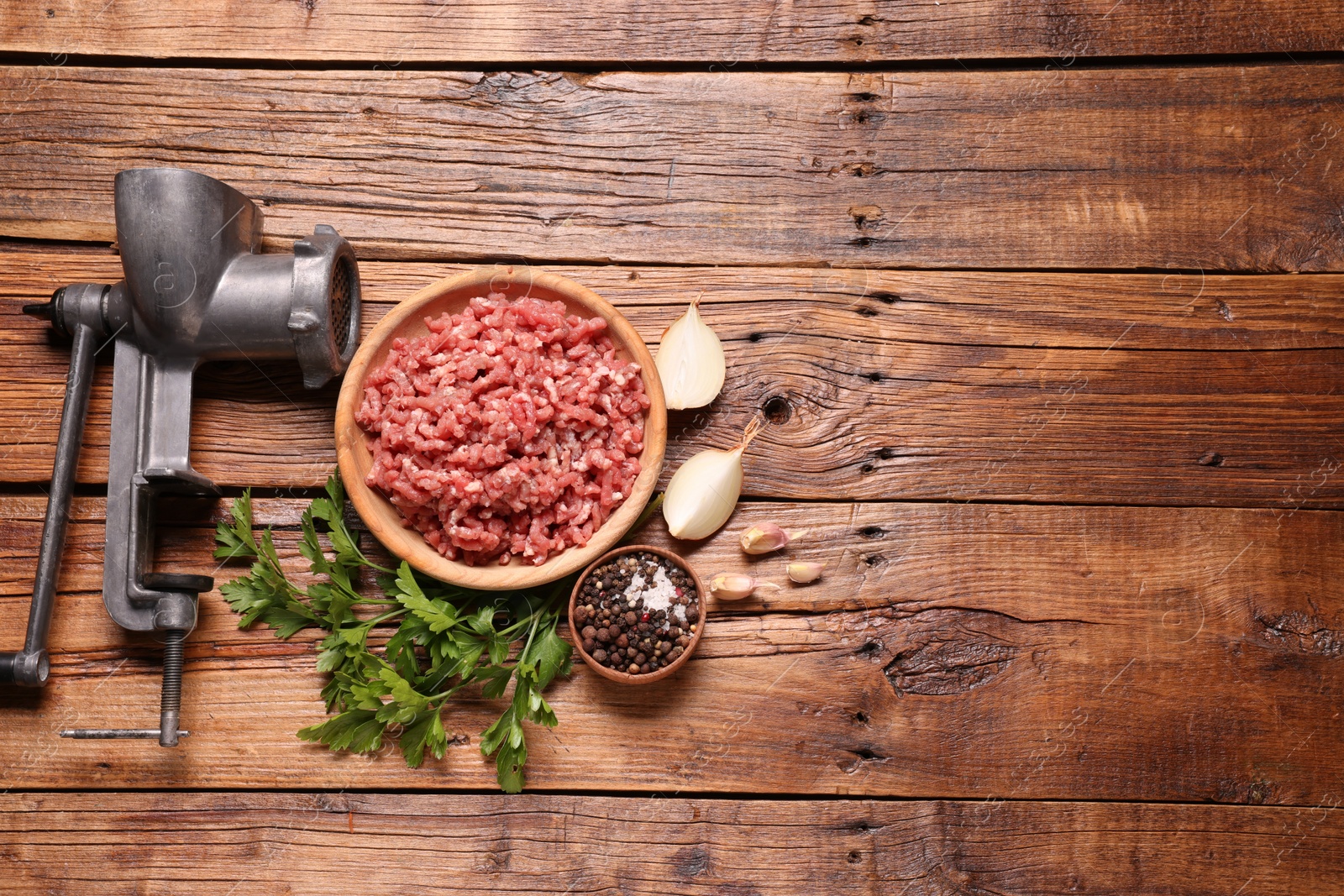 Photo of Manual meat grinder with beef mince, peppercorns, onion and parsley on wooden table, flat lay. Space for text