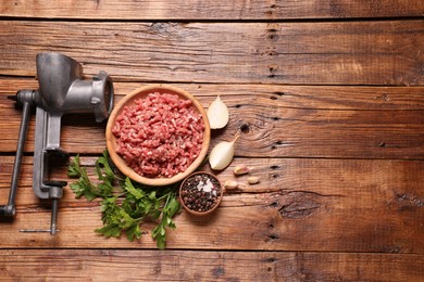 Photo of Manual meat grinder with beef mince, peppercorns, onion and parsley on wooden table, flat lay. Space for text