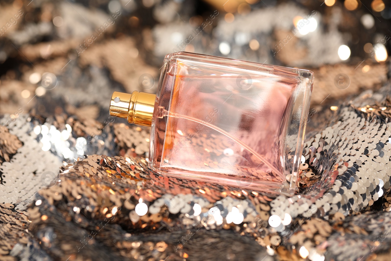 Photo of Luxury perfume in bottle on fabric with shiny sequins, closeup