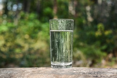 Photo of Glass of cool water on wooden surface outdoors