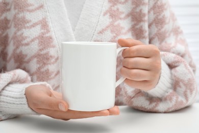 Photo of Woman holding mug at white table, closeup. Mockup for design