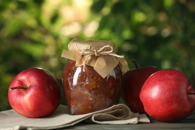Photo of Glass jar with delicious apple jam and fresh fruits on wooden table against blurred background, closeup