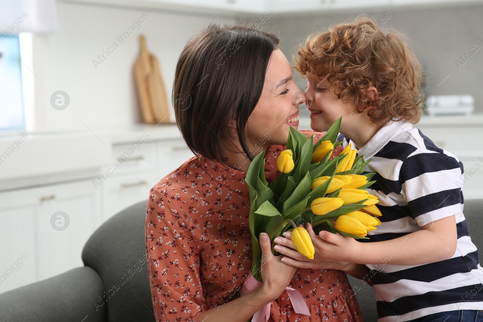 Photo of Little son congratulating his mom with Mother`s day at home. Woman holding bouquet of yellow tulips