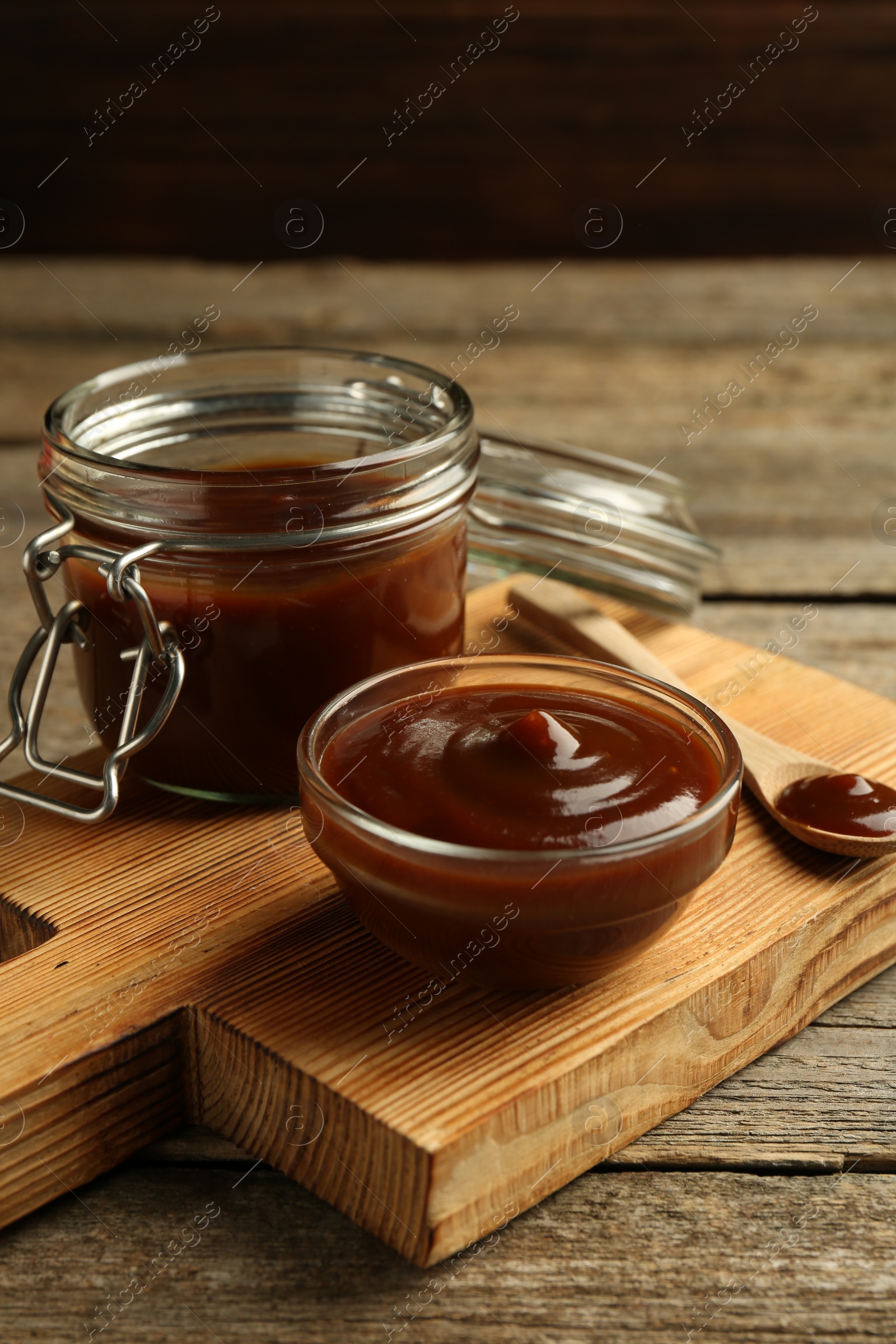 Photo of Tasty barbeque sauce in bowl, jar and spoon on wooden table