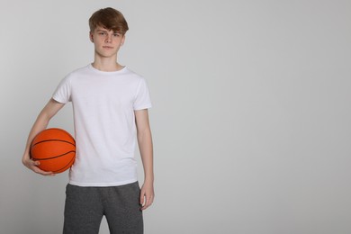 Photo of Teenage boy with basketball ball on light grey background. Space for text