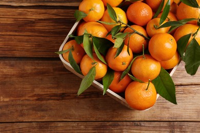 Fresh tangerines with green leaves in crate on wooden table, top view. Space for text