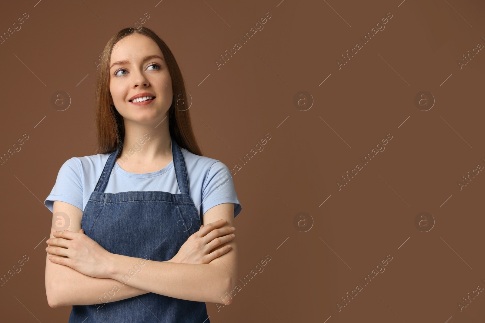 Photo of Beautiful young woman wearing kitchen apron on brown background. Mockup for design