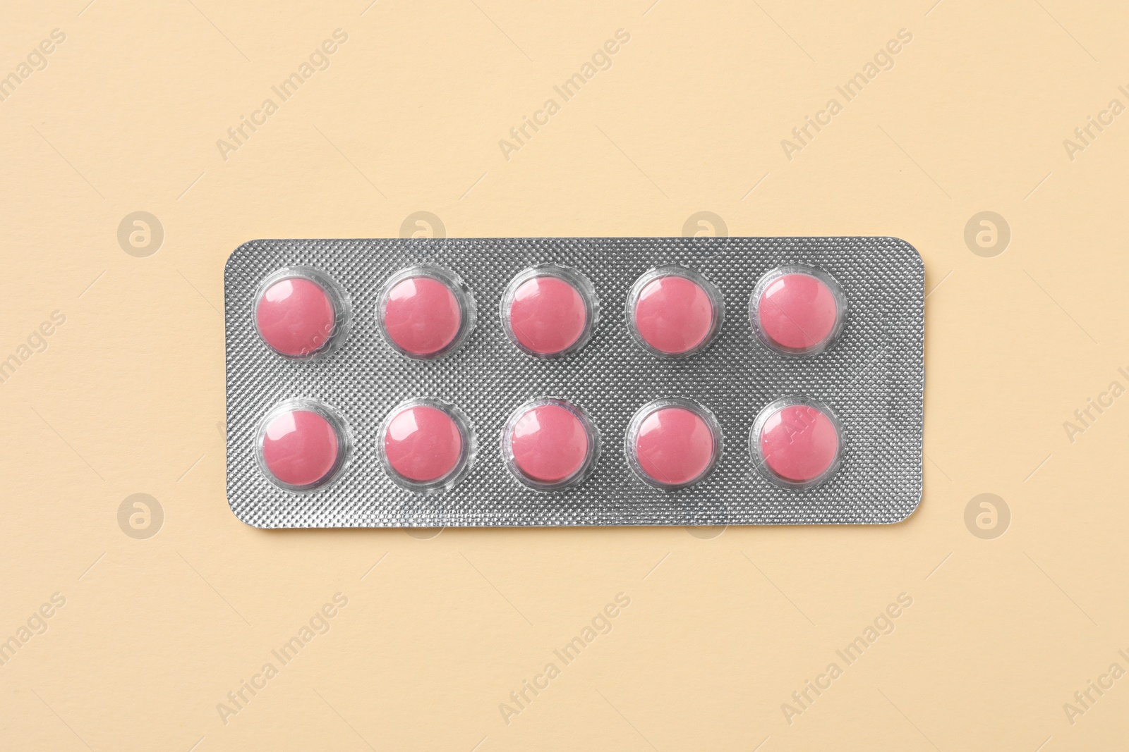 Photo of Pink pills in blister on beige background, top view