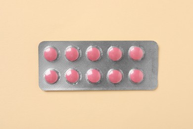 Photo of Pink pills in blister on beige background, top view