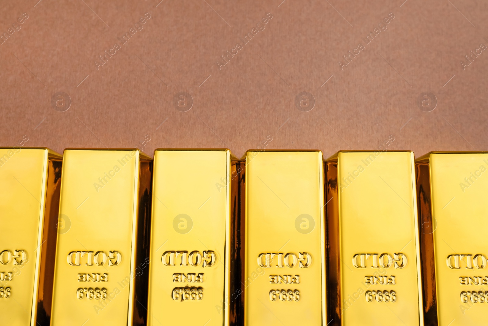 Photo of Many shiny gold bars on brown background, top view with space for text