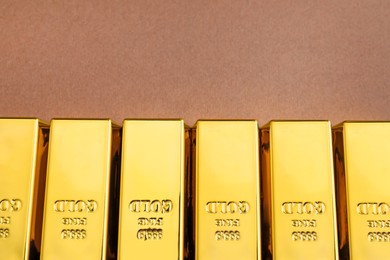 Many shiny gold bars on brown background, top view with space for text