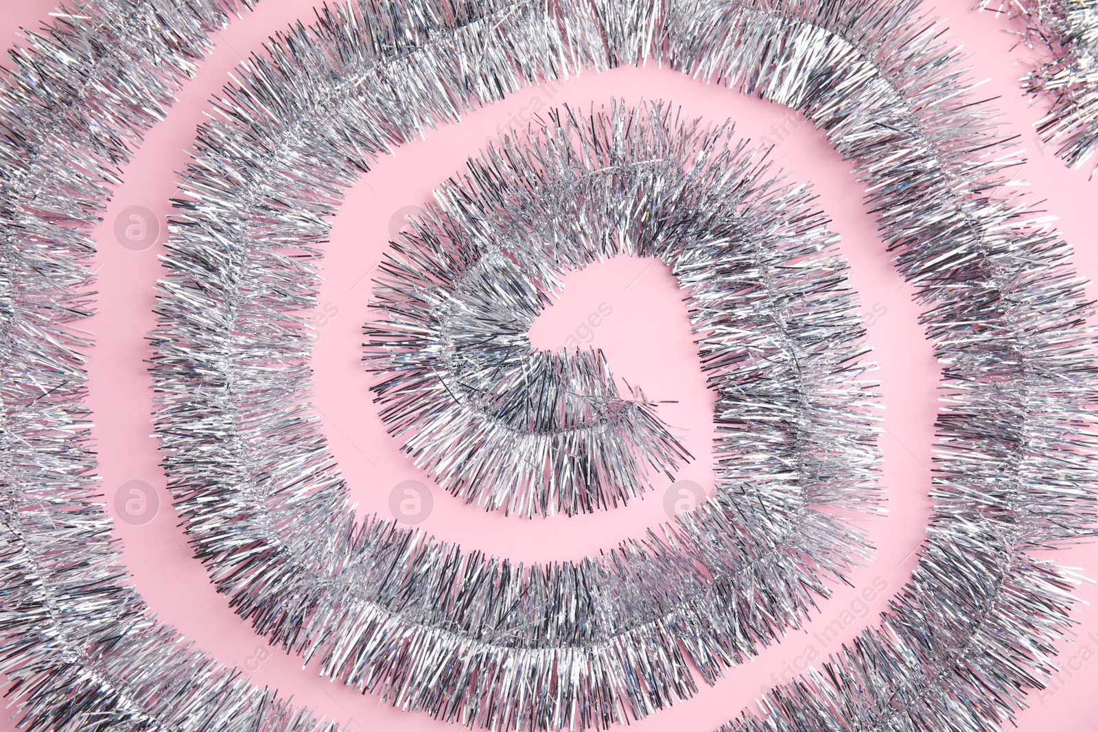 Photo of Spiral of silver tinsel on pink background, top view