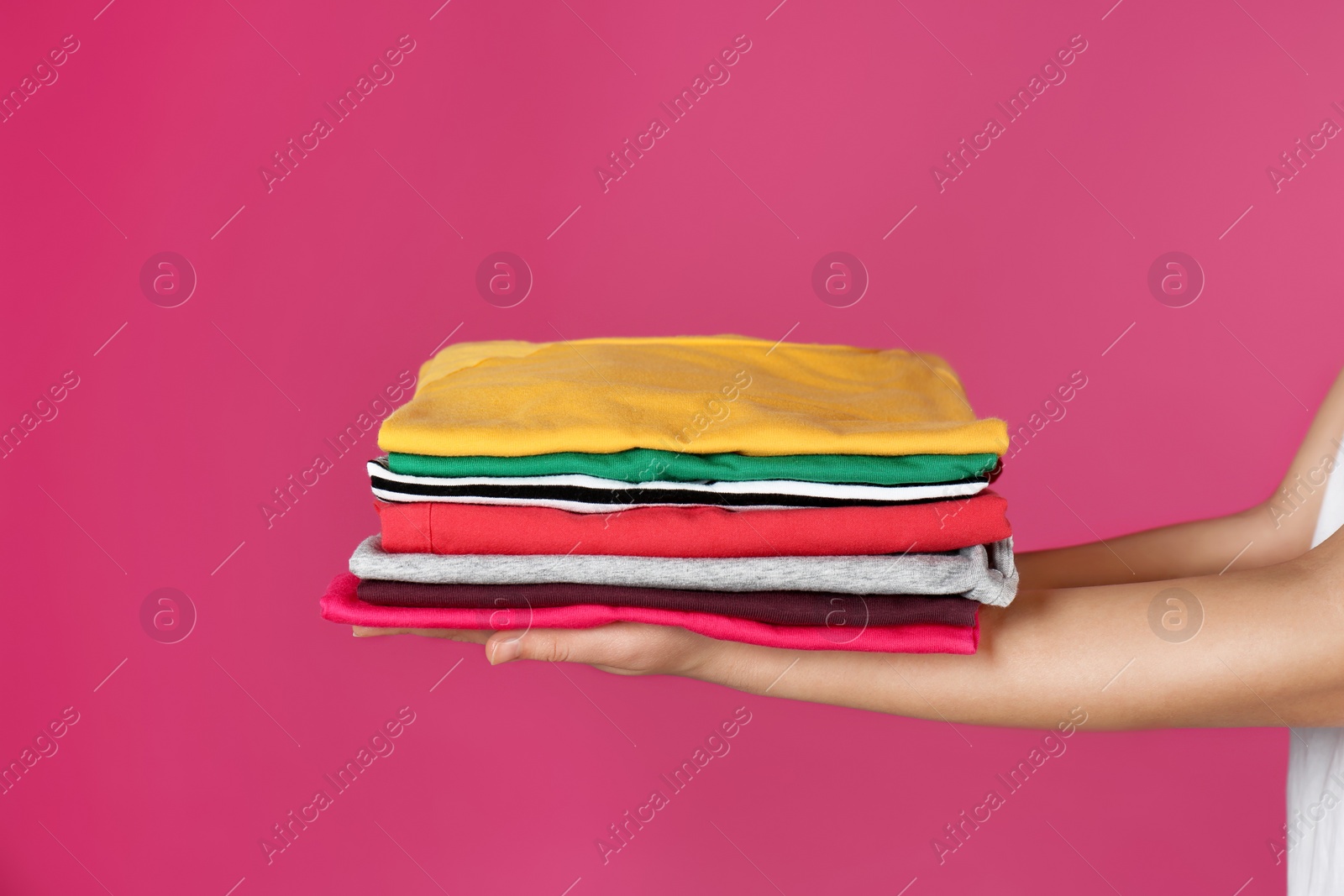 Photo of Young woman holding clean laundry on color background, closeup