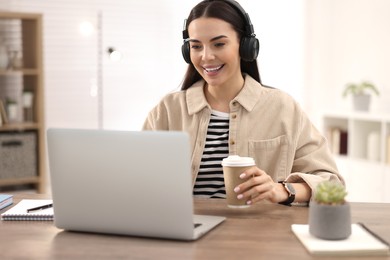 Young woman in headphones watching webinar at table in room