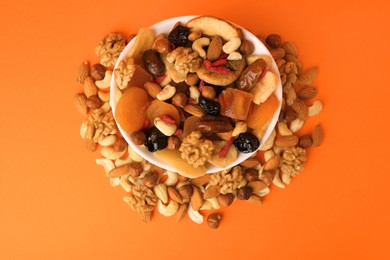 Bowl with mixed dried fruits and nuts on orange background, flat lay