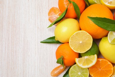 Different citrus fruits with fresh leaves on white wooden table, flat lay. Space for text