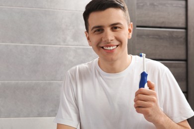 Photo of Happy man with electric toothbrush in bathroom
