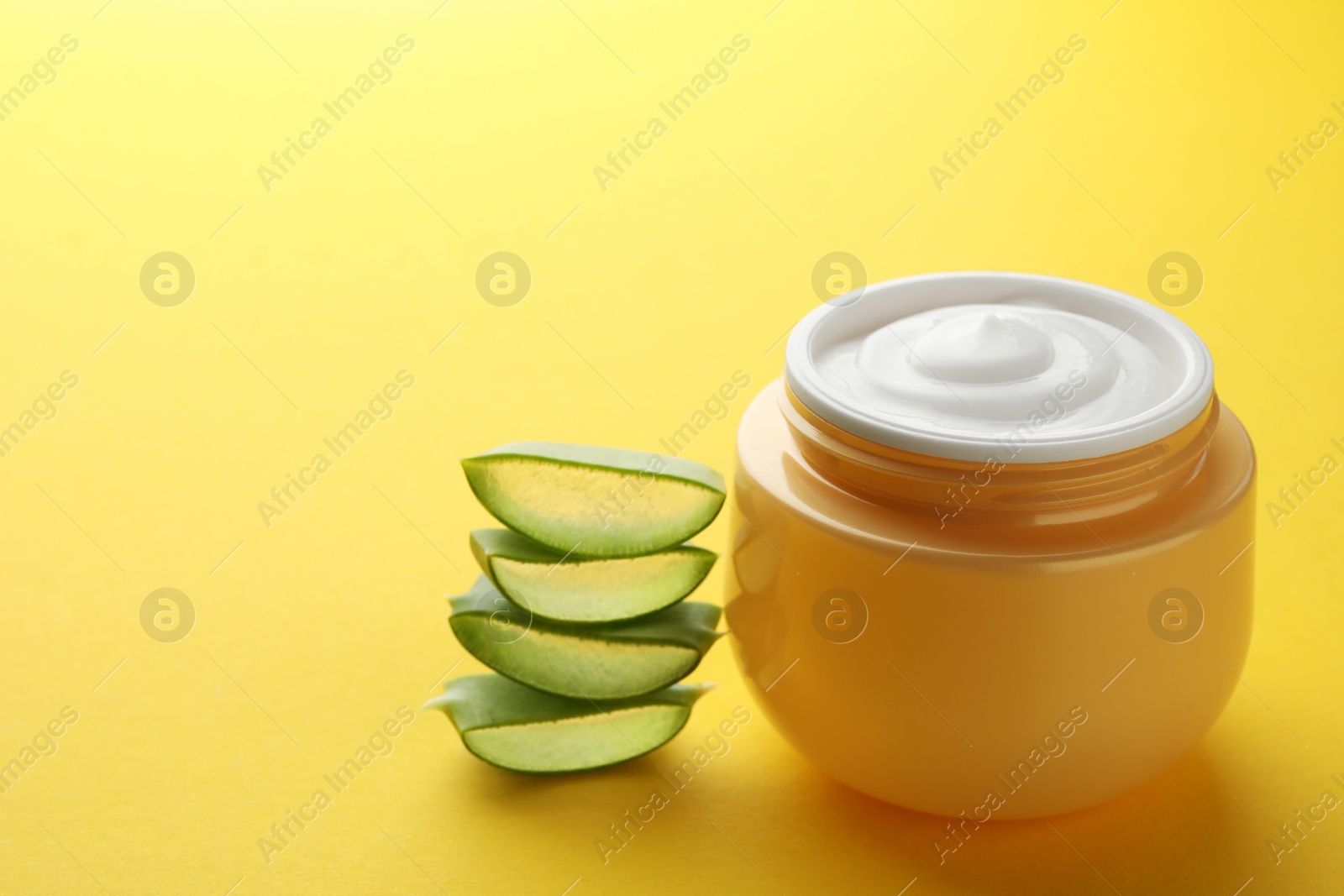 Photo of Jar with cream and cut aloe leaf on yellow background, closeup. Space for text