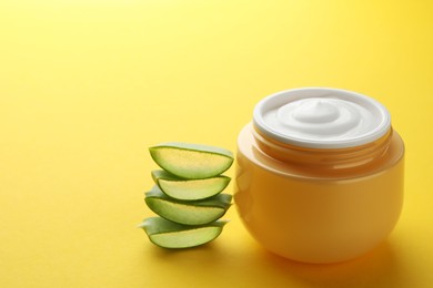 Jar with cream and cut aloe leaf on yellow background, closeup. Space for text