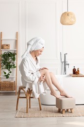Photo of Beautiful young woman applying body spray onto legs in bathroom
