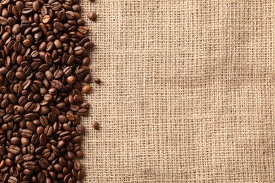 Photo of Many coffee beans on burlap fabric, top view. Space for text