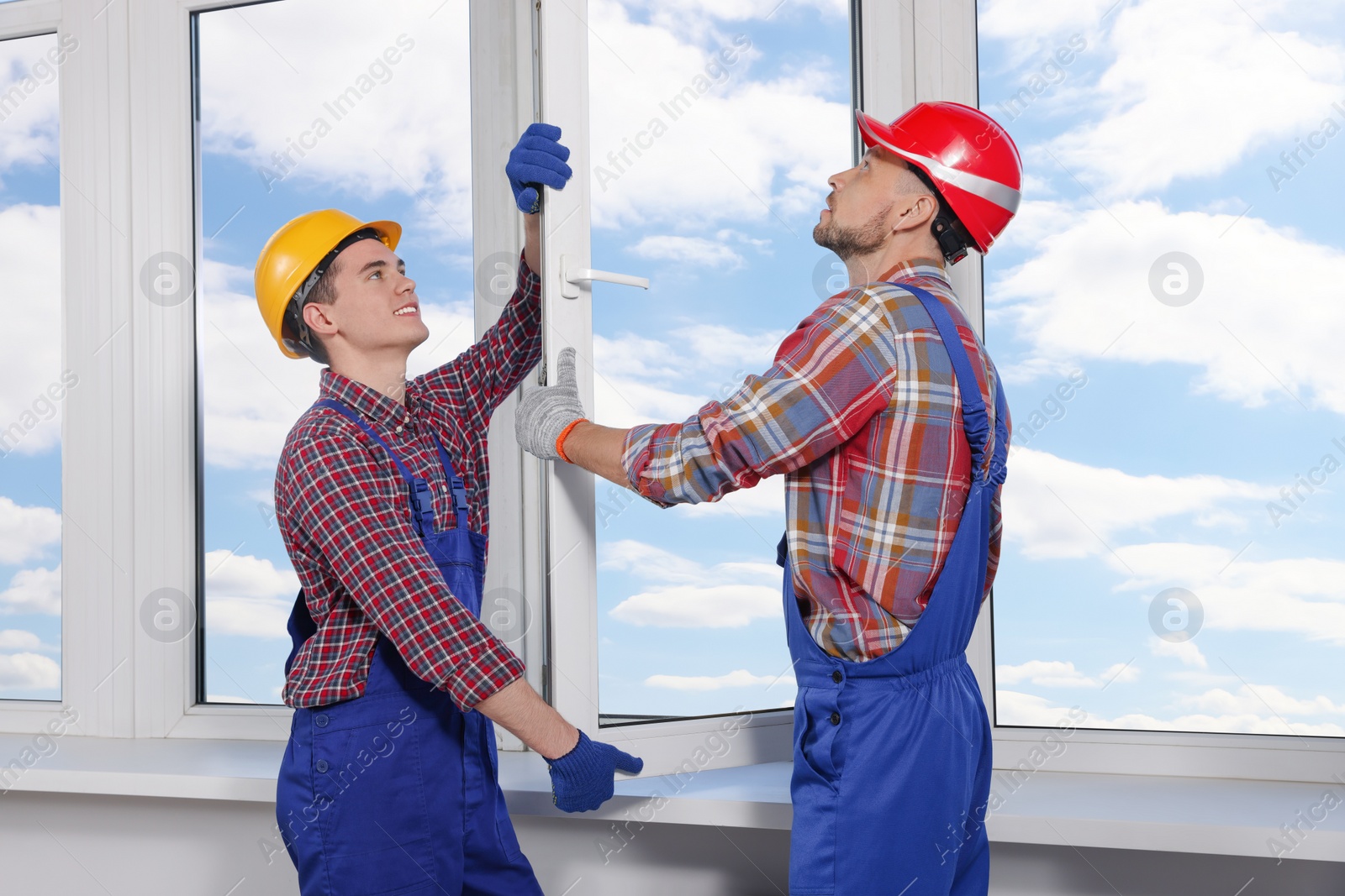 Photo of Workers in uniform installing plastic window indoors