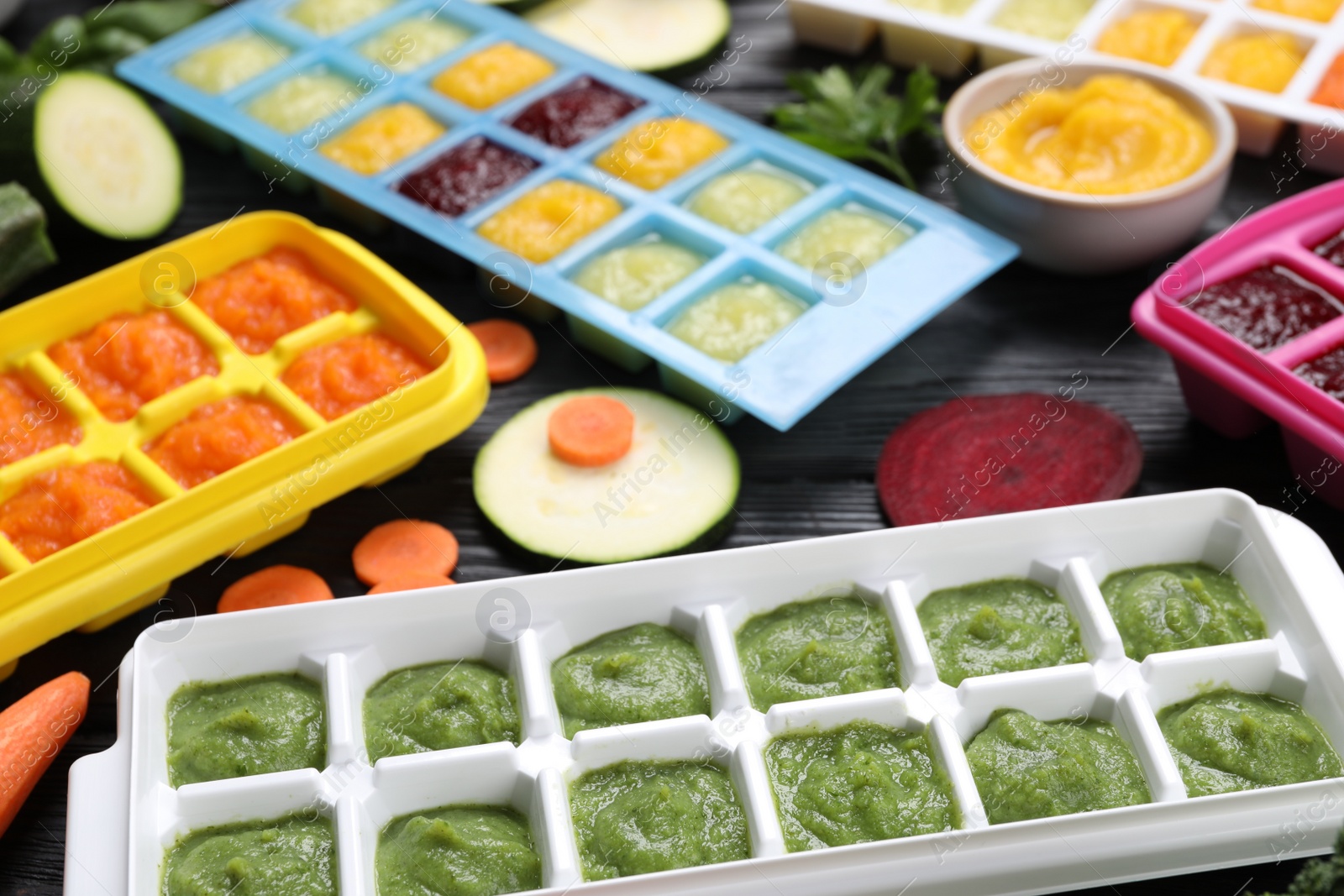 Photo of Different frozen purees in ice cube trays and ingredients of black wooden table. Ready for freezing