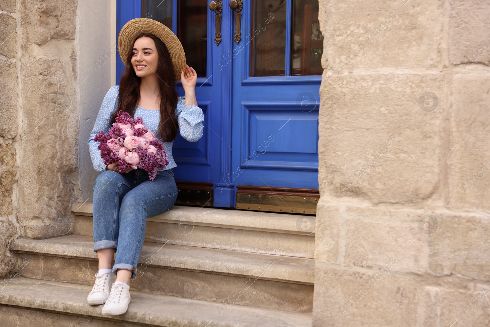 Photo of Beautiful woman with bouquet of spring flowers on stairs near building, space for text