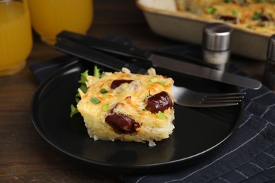 Photo of Tasty sausage casserole with green onions and cutlery served on wooden table, closeup