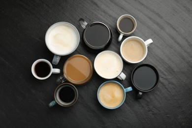 Photo of Different coffee drinks in cups on dark textured table, flat lay