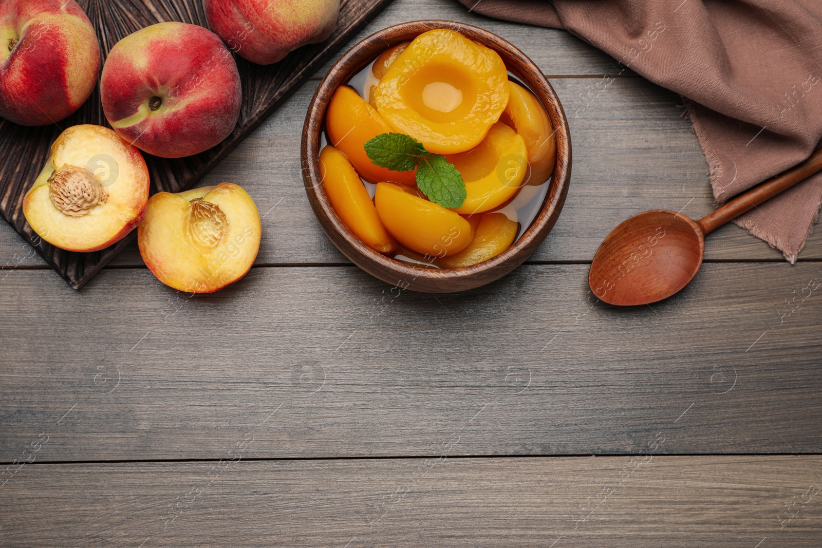 Photo of Canned peach halves in bowl on wooden table, flat lay. Space for text