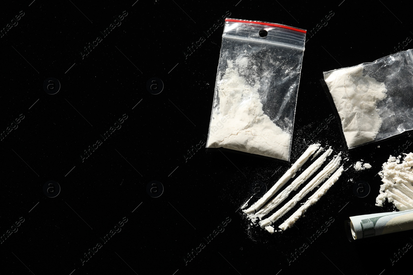 Photo of Plastic bags with hard drug and rolled dollar banknote on black background, flat lay. Space for text