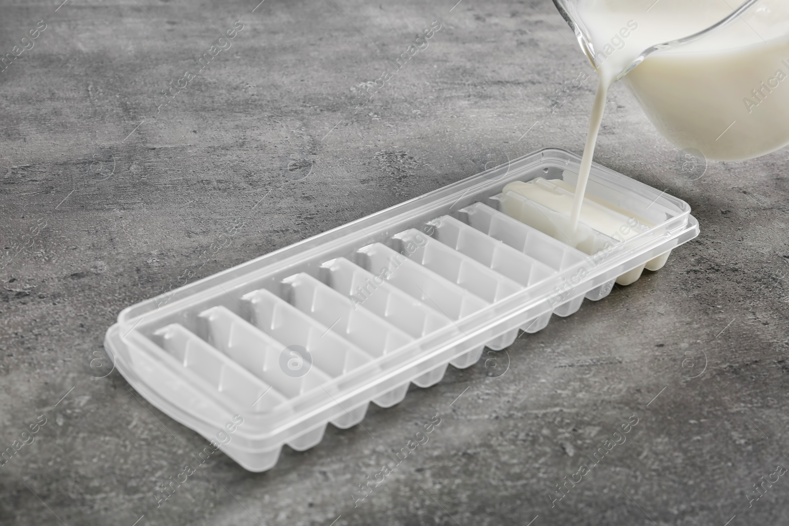 Photo of Pouring milk into ice cube tray on grey table