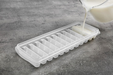 Pouring milk into ice cube tray on grey table