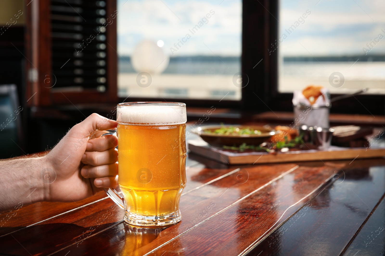 Photo of Man with glass of tasty beer at wooden table in pub, closeup. Space for text