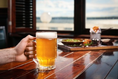 Photo of Man with glass of tasty beer at wooden table in pub, closeup. Space for text
