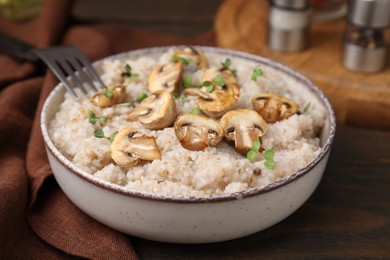 Photo of Delicious barley porridge with mushrooms and microgreens in bowl on table, closeup