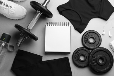 Photo of Flat lay composition with sportswear, notebook and equipment on grey table. Gym workout plan