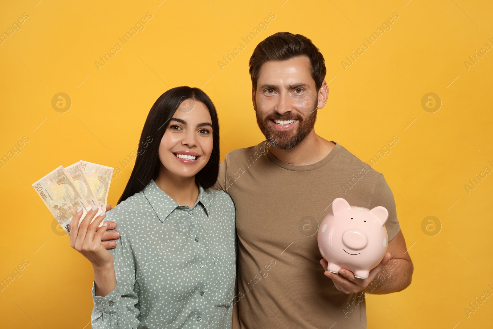 Photo of Happy couple with ceramic piggy bank and money on orange background