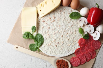 Pizza base and products on light textured table, top view