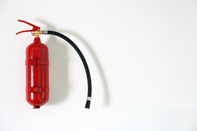 Fire extinguisher hanging on white wall, space for text