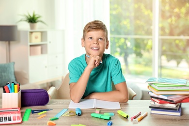 Cute boy doing homework at table with school stationery indoors