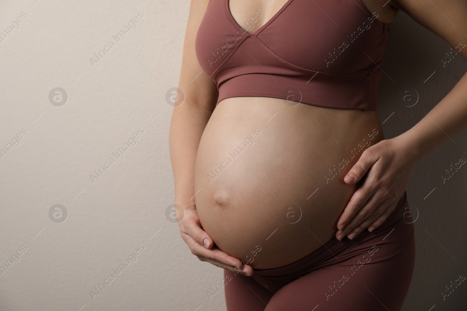 Photo of Pregnant young woman touching belly on beige background, closeup. Space for text