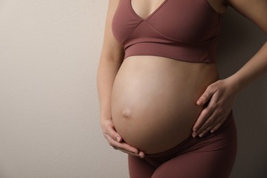 Pregnant young woman touching belly on beige background, closeup. Space for text