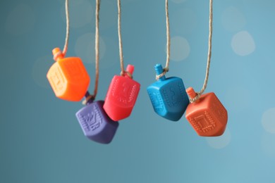 Photo of Hanukkah celebration. Plastic dreidels with jewish letters hanging on twine against light blue background with blurred lights, closeup