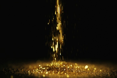 Photo of Sprinkling gold glitter on black background, bokeh effect