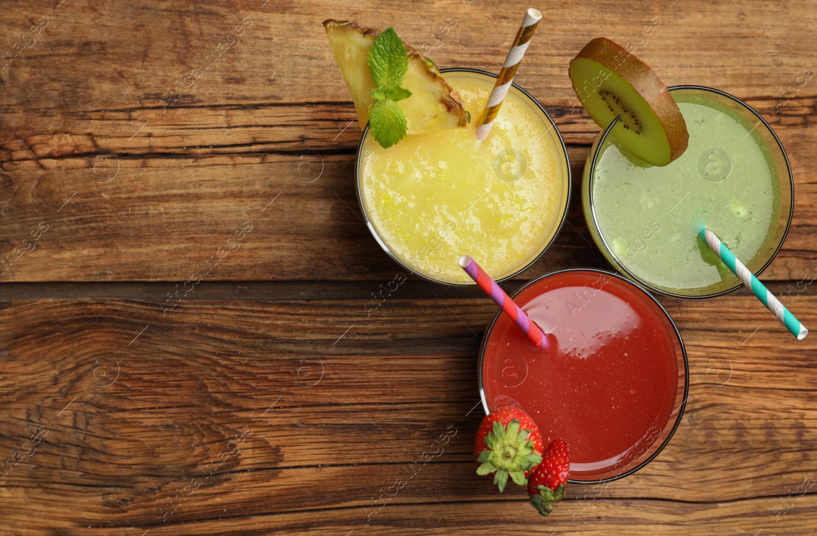 Photo of Delicious colorful juices in glasses on wooden table, flat lay. Space for text