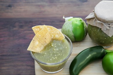 Photo of Delicious salsa sauce with tortilla chips and ingredients on wooden table, closeup