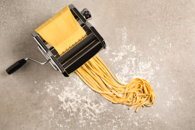Photo of Pasta maker machine with dough on grey table, top view