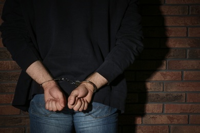 Male criminal in handcuffs near brick wall, closeup